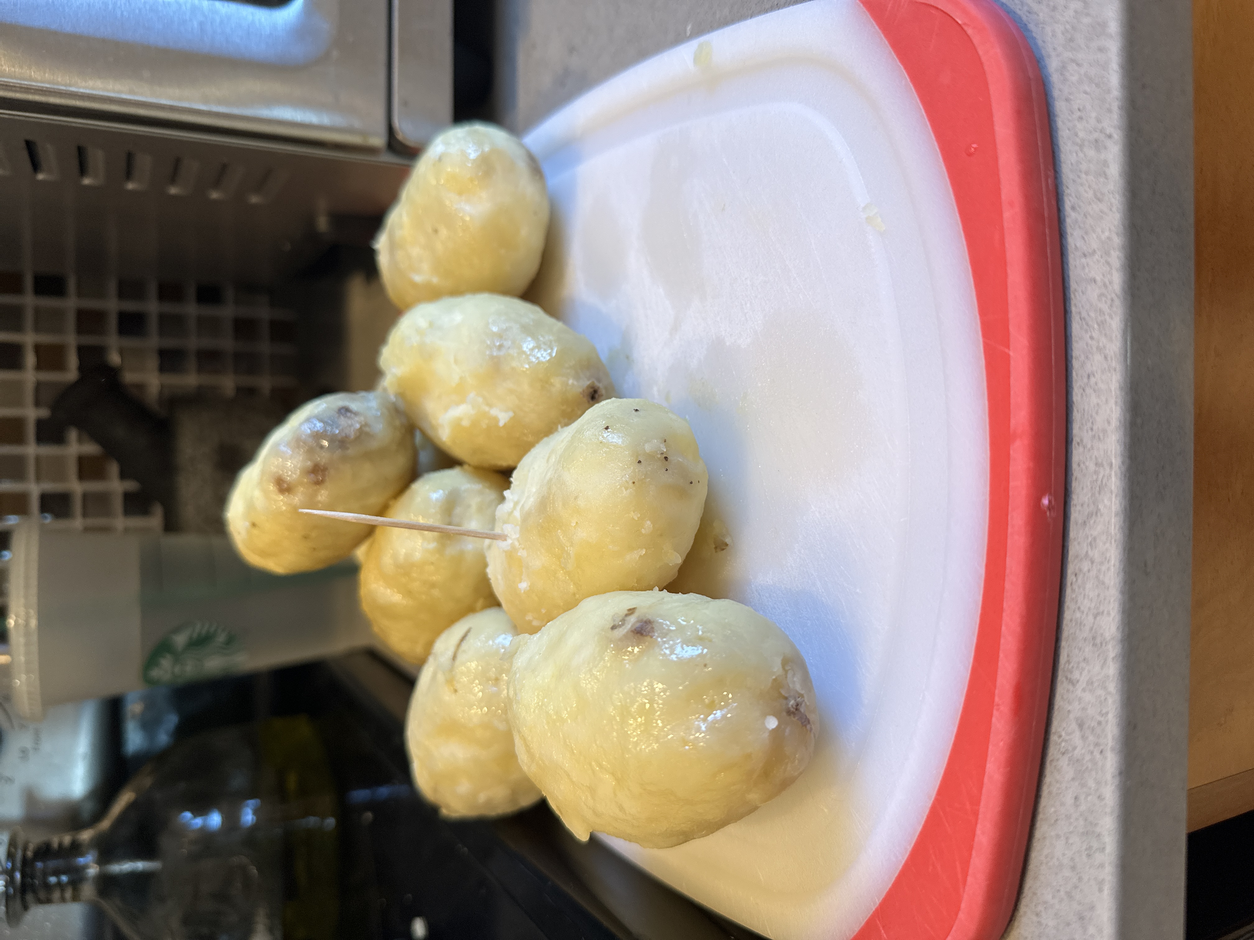 Peeled, oiled russet potatoes on a cutting board with a toothpick mid-poke