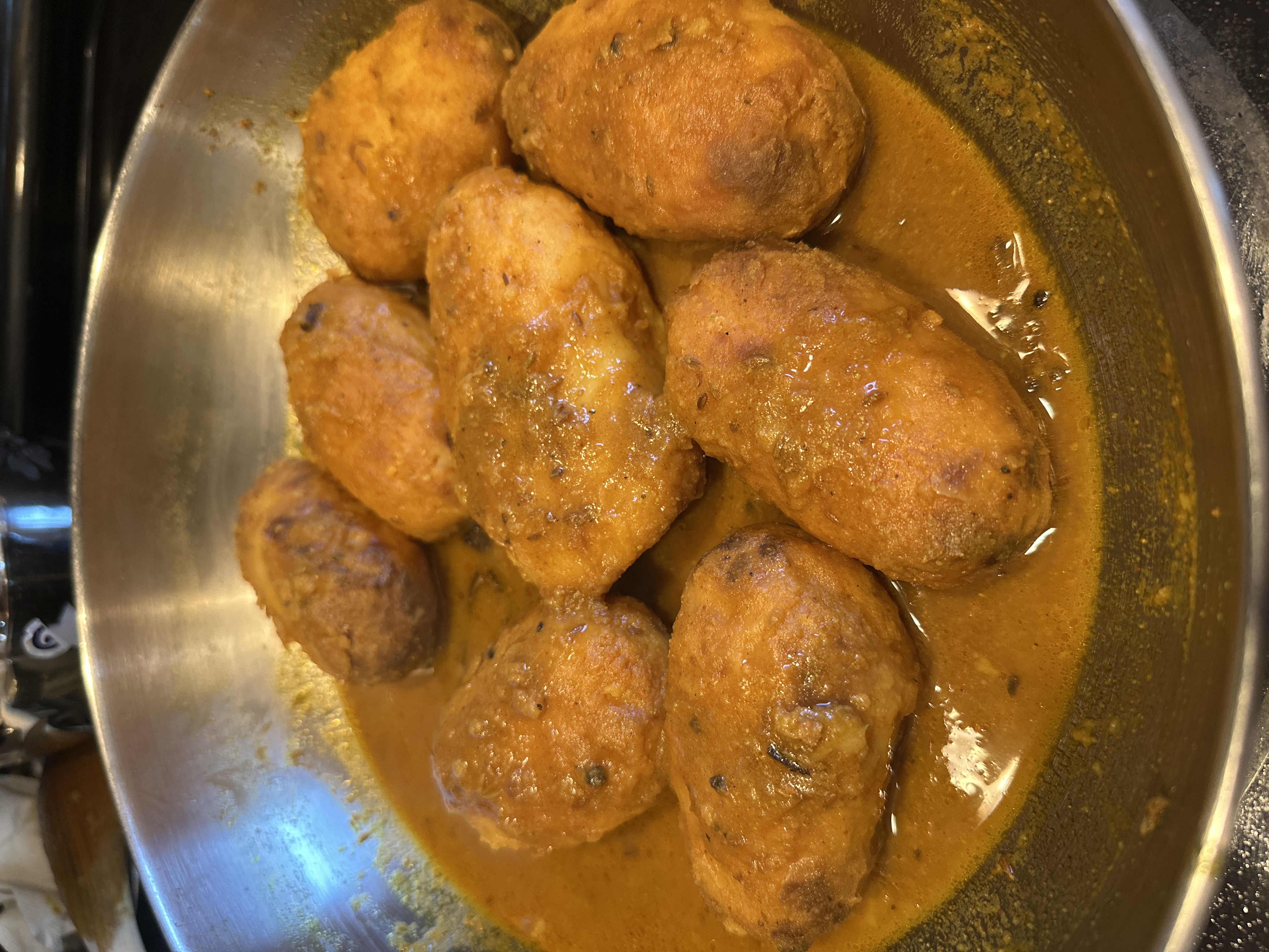 Finished Dum Aloo in a deep brick-red rass sauce