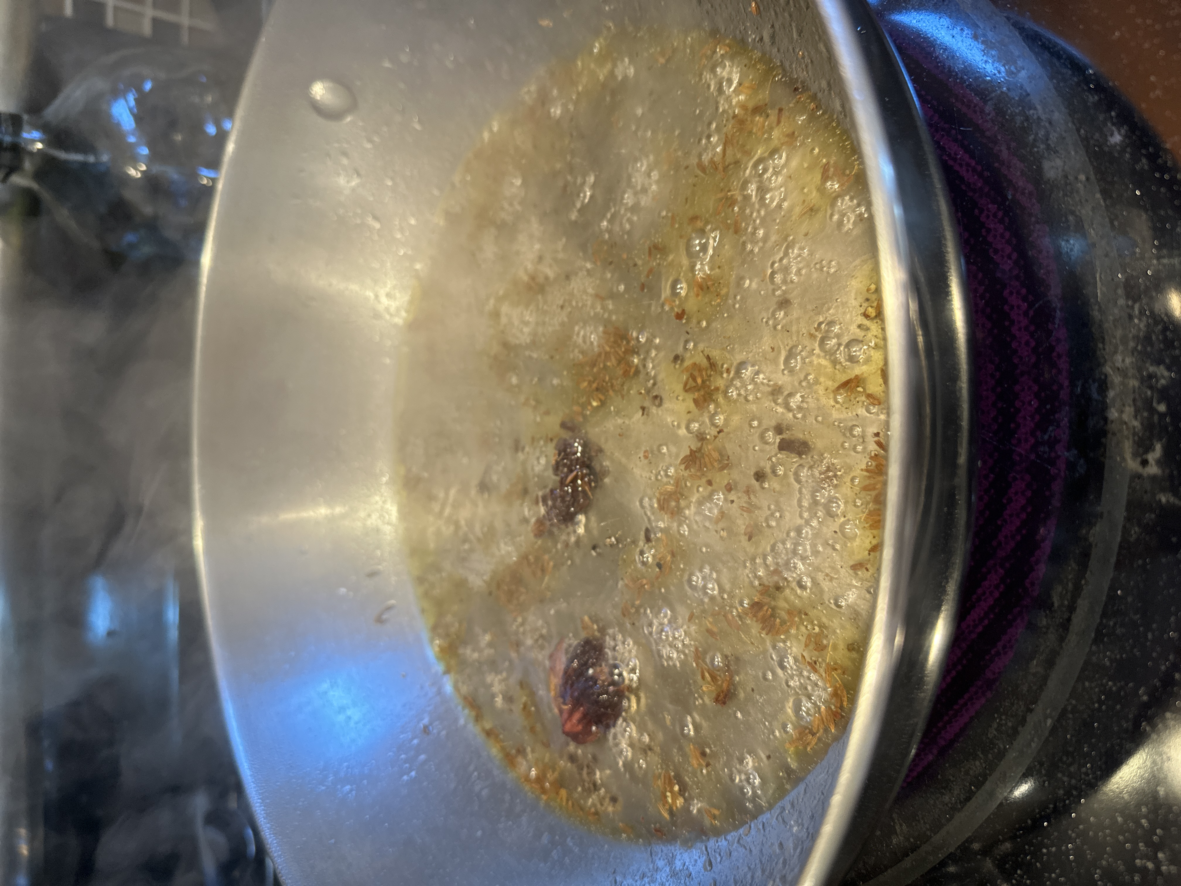 Cumin seeds, hing, and black cardamom sputtering in hot oil